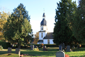 Gräber auf Wiese zwischen Bäumen vor Kirche